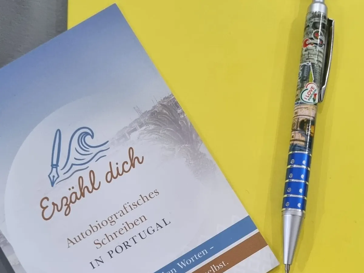 Gelbes Notizbuch mit Kugelschreiber und dem Programmheft „Erzähl dich – Autobiografisches Schreiben in Portugal“
