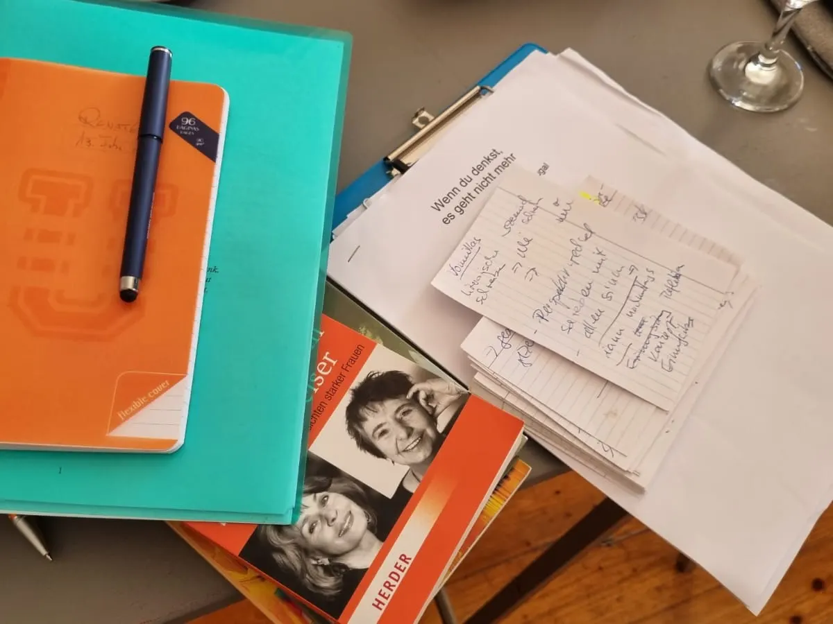 Schreibtisch mit Notizheft, Stift, Notizzetteln und aufgeschlagenen Büchern