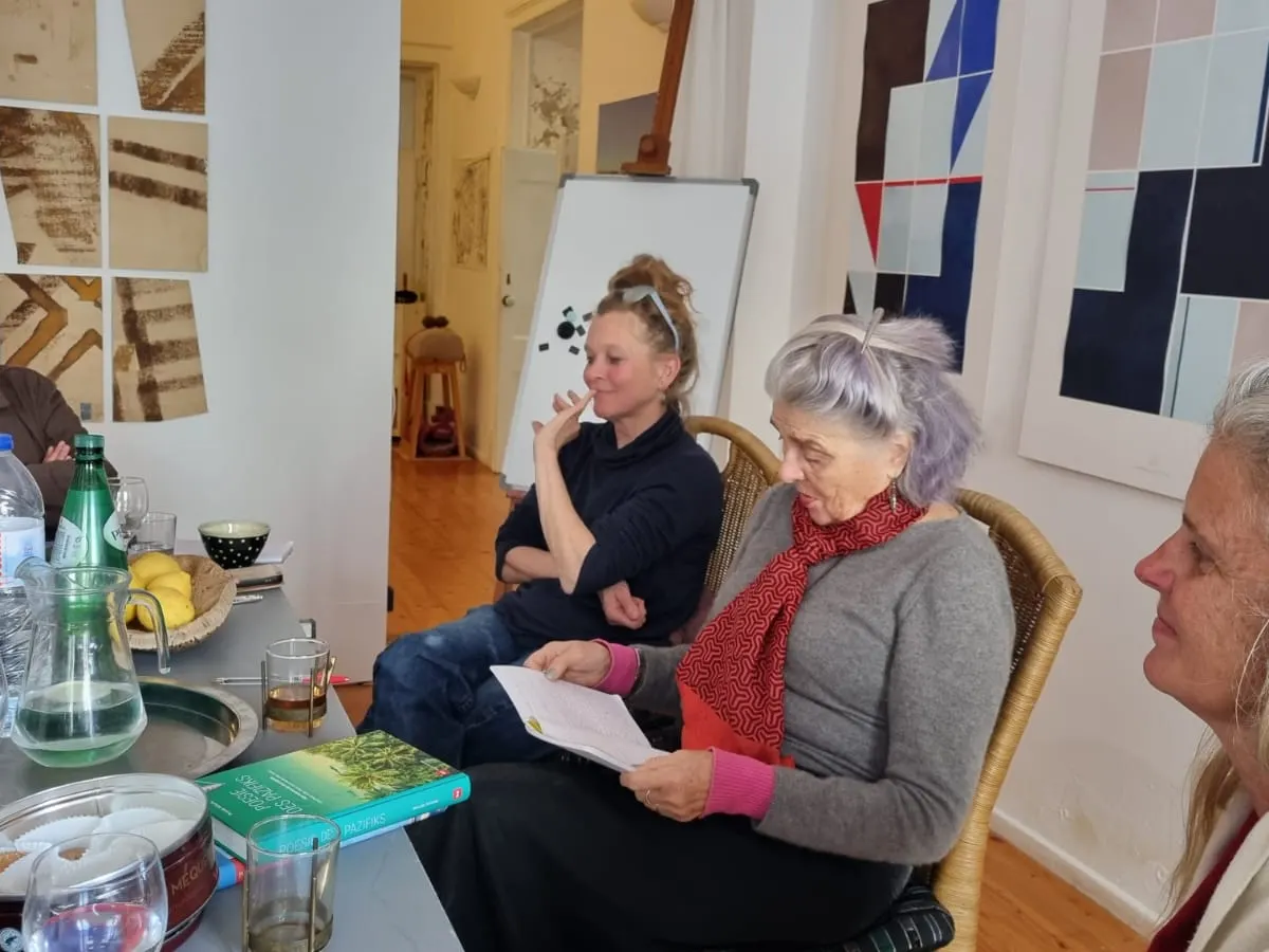 Workshop-Runde in einem hellen Raum: Teilnehmerinnen und Teilnehmer sitzen um einen Tisch, eine Frau liest aus ihrem Text vor
